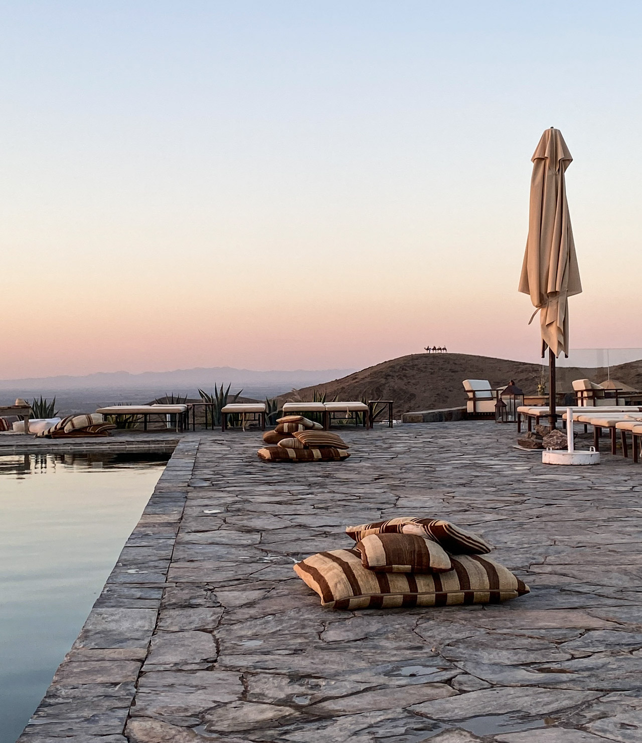Poolrand mit Kissen und Sonnenschirm in der White Camel Lodge bei Sonnenuntergang