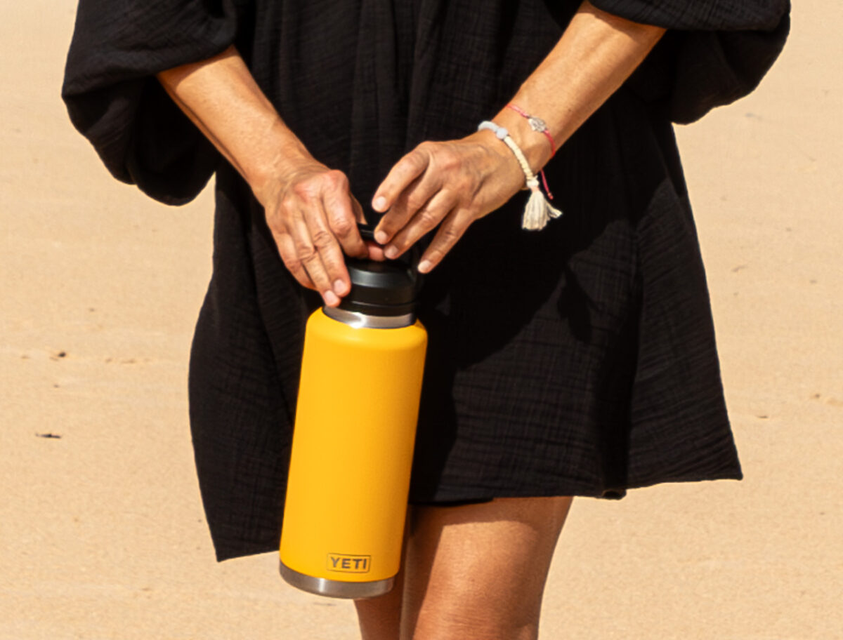 Person mit gelber Yeti Tumbler Bottle im Wüstensand